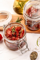 Food recipe background. Close up Sun dried tomatoes with garlic, oregano, olive oil in a jar on a light table.