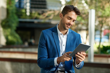 Smiling young businessman standing outside using a digital tablet