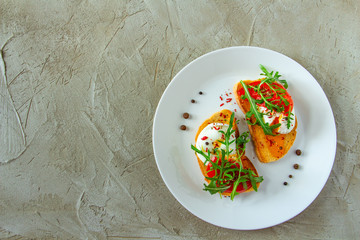 delicious poached eggs on crispy slices of wheat bread with slices of tomato, arugula, spices and black pepper on a white plate on a concrete background