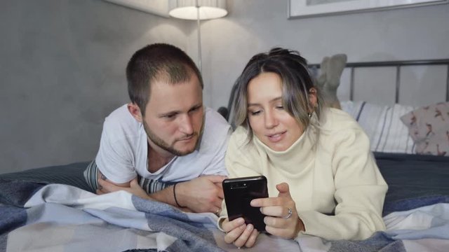 Man and woman are lying in bed before sleep, using their smartphones, showing pictures