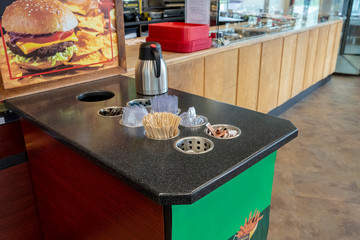 Close-up view of various disposable wooden sticks, plastic utensils, spices, tooth sticks and sugar bags on wooden counter in cafe for self-service and take away drinks.