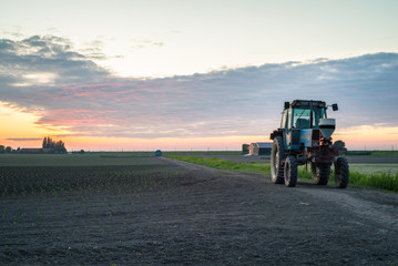 Fototapeta premium Tractor is parked on an agricultural field with beautiful colored clouds in the background