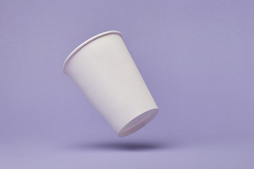 White paper cup of coffee colored background.  Flying paper cup on violet background. Isolated for mock up
