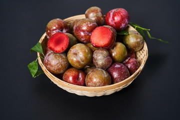 Fresh plums in a woven bamboo basket against a black background