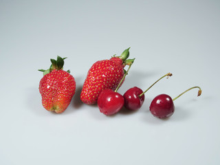 a pair of strawberries and cherries lie on a monotonous table