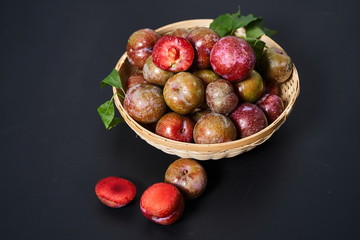 Fresh plums in a woven bamboo basket against a black background