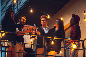 Corporate celebrating in the warm light of the lamps in summer evening, young friends, colleagues...