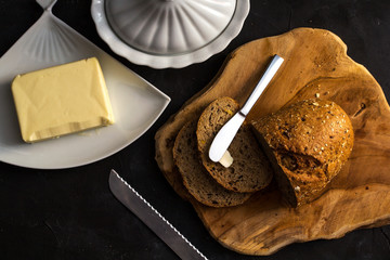 Loaf of bread with butter and knife. Dark background. top view