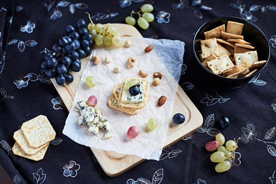 Three Blue Cheese Crackers With Grapes Are On A Cutting Board.