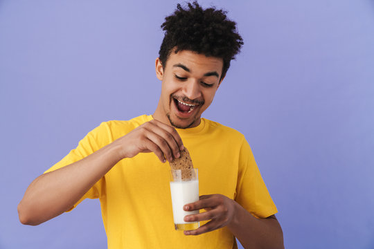 Photo of african american man smiling while eating cookie with milk