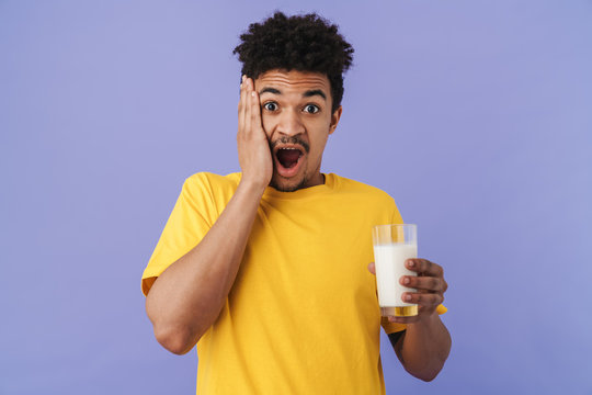 Photo of shocked african american man holding glass with milk