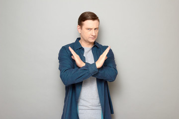 Portrait of serious man making cross with hands, showing stop gesture