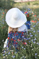 Dama w białym kapeluszu na łące pośród kwiatów
