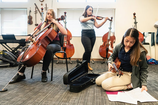 Teenage girls rehearsing violins and cello in classroom