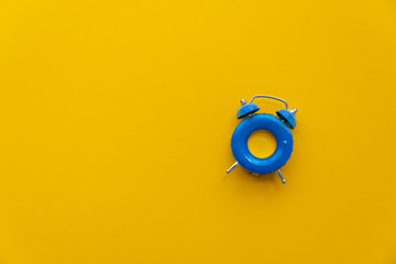 Vacation time. Blue alarm clock as swimming ring form on yellow background. Top view. Copy space