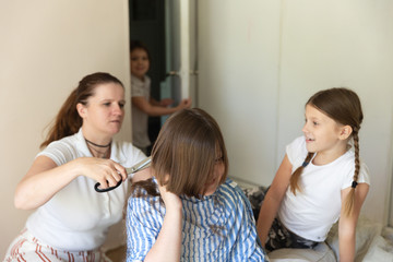 Caucasian mom cuts her kid at home, siblings look