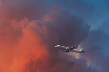 Commercial airplane flying through clouds in dramatic sunset light. Travel concept. Soft focus. Toned