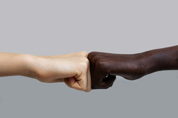 The black African-American hand and the white European hand give a blow to the partnership and cooperation agreement against a grey isolated background.The concept of combating racism
