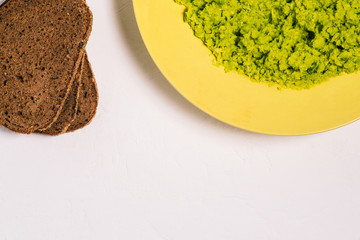 Plate of mashed avocado and slices of sliced bread on a white table with a copy of the space. Recipe for avocado toast. A top view of a flat layout.