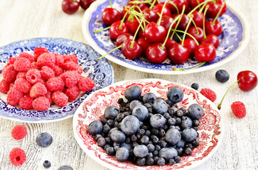 Red and blue berries - forest blueberries, blueberries, raspberries, cherries in a  dish with a red and blue pattern.  Summer berries. Soft focus
