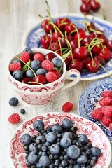 Red and blue berries - forest blueberries, blueberries, raspberries, cherries in a  dish with a red and blue pattern.  Summer berries. Soft focus