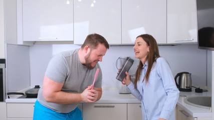 Obraz premium Chubby man and woman dancing and singing in the kitchen while cooking at home, the concept of a happy fun family