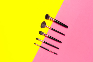 Professional makeup brushes on bright yellow pink background flat lay top view copy space. Beauty product, women's accessory, fashion. Different brushes for decorative makeup. Cosmetic makeup Set