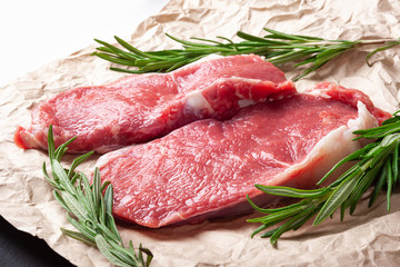 Raw meat . Two slices of fresh raw meat and a branch of rosemary on paper. Preparing meat for a barbecue.