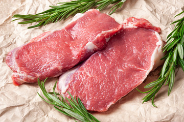 Raw meat . Two pieces of fresh raw meat and a branch of rosemary on paper. Preparing meat for a barbecue.