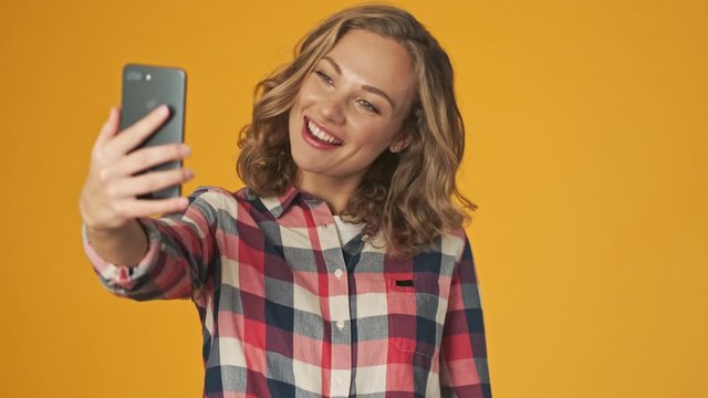 Young happy girl isolated over yellow wall background take a selfie by mobile phone