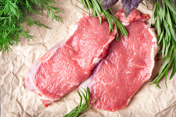 Raw meat and rosemary. Top view of two slices of fresh raw meat, rosemary on paper. Preparing meat for a barbecue.