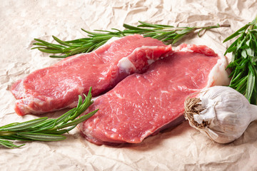 Raw meat and garlic. Two pieces of fresh raw meat, garlic and rosemary on paper. Preparing meat for a barbecue.