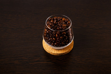 Fototapeta na wymiar Glass goblet with coffee beans is isolated on a wooden background on a cork wood stand.