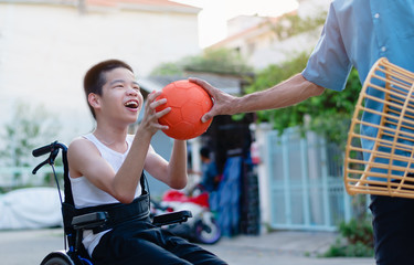 Fototapeta premium A ball in hands the parent and Asian special child on wheelchair, They playing chair ball to strengthen muscles in the house, Lifestyle of disabled child, Happy disability kid stay at home concept.