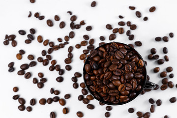 Coffee beans sprinkled in a black glass coffee cup isolated on a white background. Coffee beans are scattered on a white background.