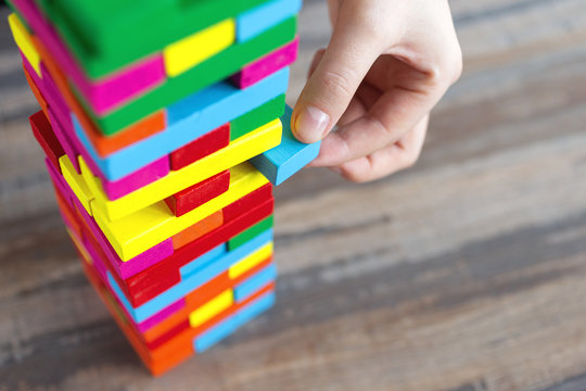 Close up of a hand pulling a colorful  jenga block from a big pile. Fun board games concept