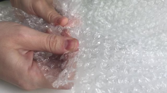 Women hands clench and slam anti-stress bubble wrap. Popping plastic bubbles. 