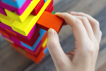 Close up of a hand pulling a colorful  jenga block from a big pile. Fun board games concept