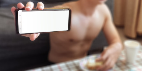 A topless Man in pants showing a blank white screen on a mobile phone while having lunch at tea table