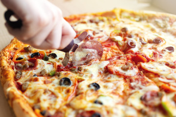 Close up of hand cutting large cheesy pepperoni pizza, background macro