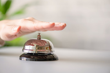 Hand of guest ringing in silver bell. reception desk with copy space. Hotel service. Selective focus