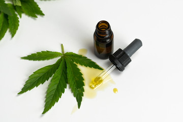 Glass bottles with CBD essential oil and medical marijuana leaf on white background, close-up. Concepts of alternative or herbal medicine