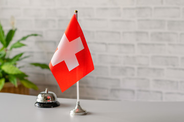Silver vintage bell with national flag of Switzerland on reception desk with copy space. Hotel service. Travel, tourism. Selective focus. Europe, Concept.
