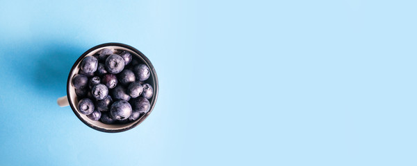 Ripe blueberry and green leaves in cup on blue surface,top view, flat lay