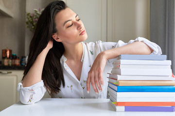 Indoor image of young woman posing at home with her reading stack of books. Smart female student rests on stack of books. Lifestyle, business and education concept