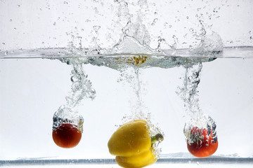 two red tomatoes and yellow pepper are falling into the water the great splash and bubbles - Powered by Adobe