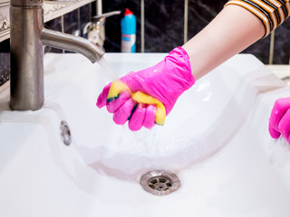 A hand in a pink glove washes a washbasin in the bathroom with a sponge with foaming detergent. Cleaning company cleans the house. Disinfection of the senile node from viruses and bacteria.
