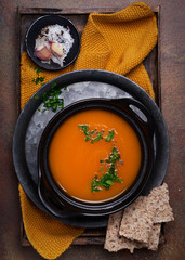 Vegetarian spicy pumpkin soup with parsley and seed crackers on dark stone table, top view, copy space. Traditional fall and winter dishes.