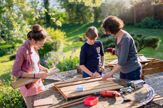 A mother and her two children build wooden planters for their permaculture vegetable garden