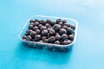Plastic container with fresh raw organic ripe blueberries on a blue background
